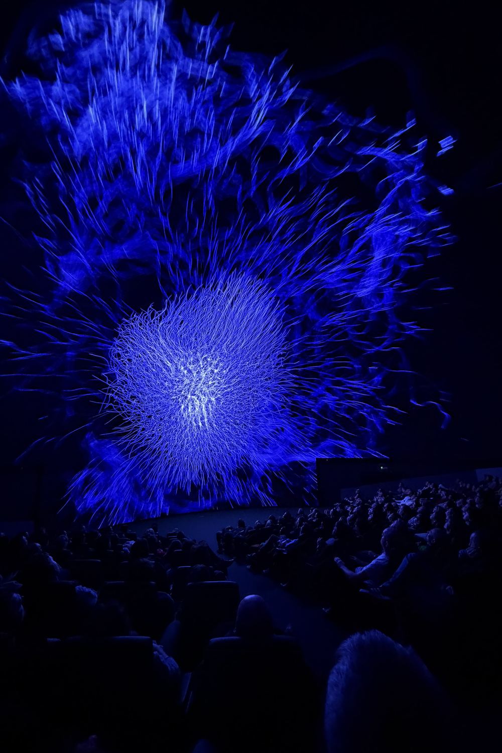 Infinite Space — radial blue particle burst with audience